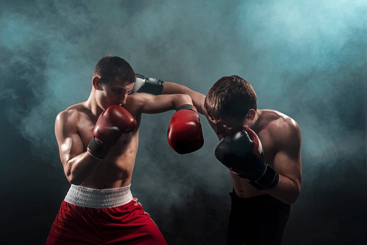 Dois lutadores de boxe a lutar no meio de um fundo nublado. Um com calções vermelhos e outro pretos